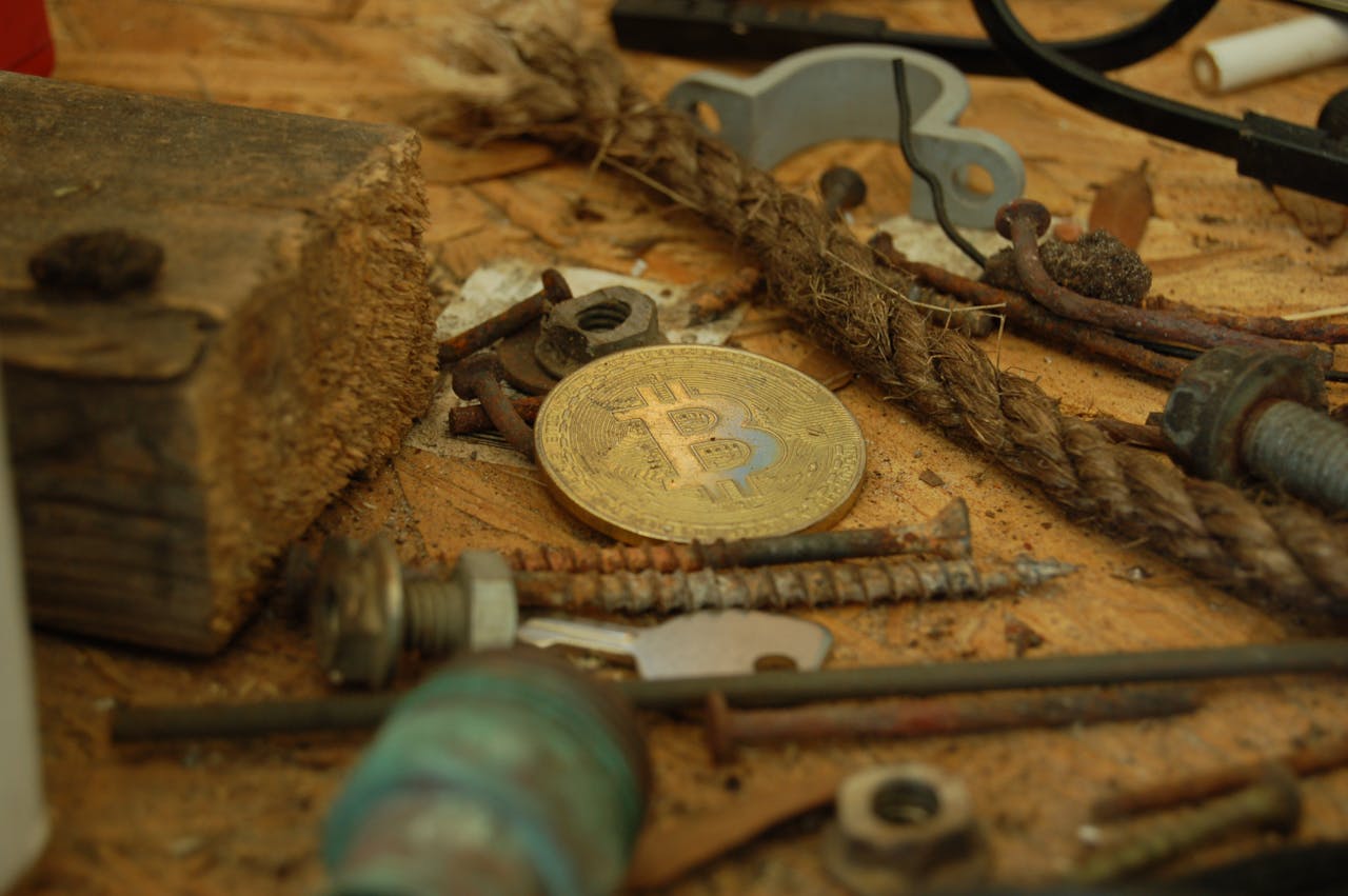 our-mission A bitcoin coin placed among various tools and hardware pieces on a wooden surface.